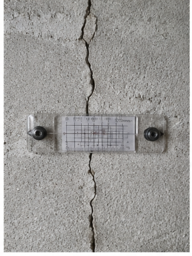 Une règle de mesure fixée sur un mur en béton fissuré.