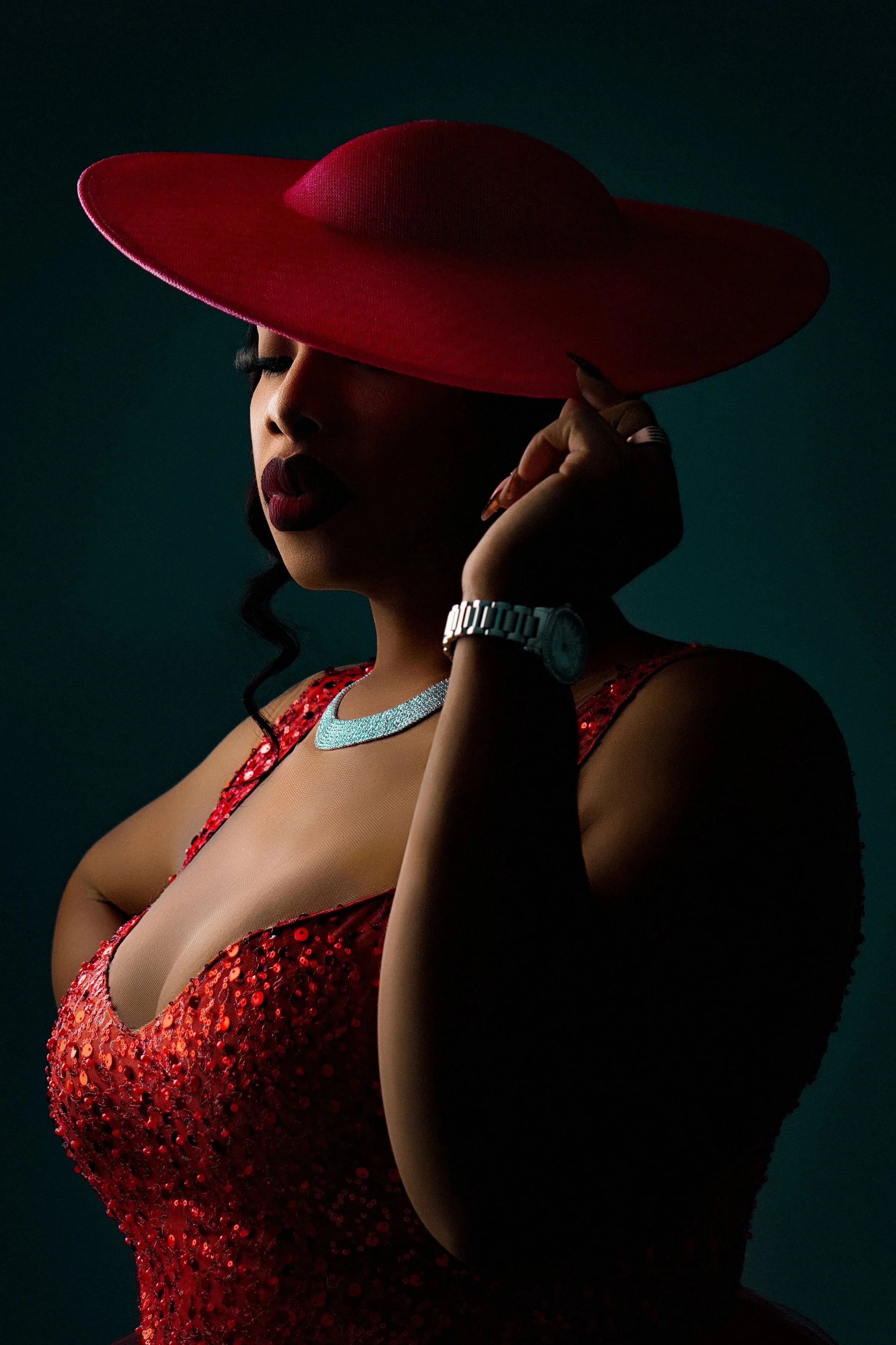 Editorial studio portrait of a woman in a red sequin dress wearing a wide-brim red hat, photographed with dramatic moody lighting at Tonya Alexis Studios in Nassau, Bahamas.