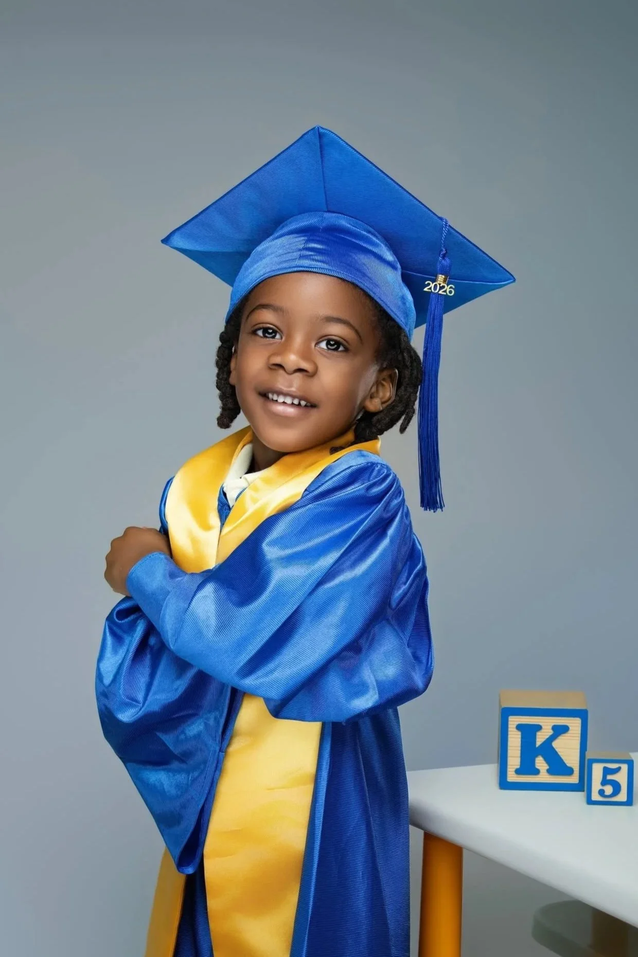 Kindergarten graduation portrait of a young boy in a blue cap and gown with a yellow Class of 2026 stole, professionally photographed by Tonya Alexis Studios in Nassau, Bahamas.