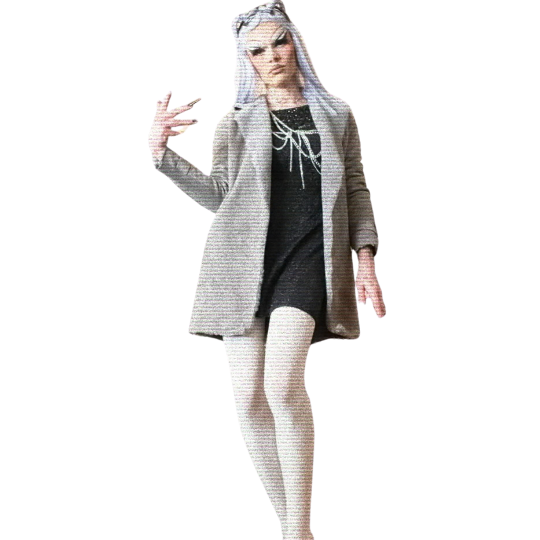 A woman with platinum blonde hair wearing a beige coat, black dress with a white bow, and white tights, posing with her hand up showing a peace sign.