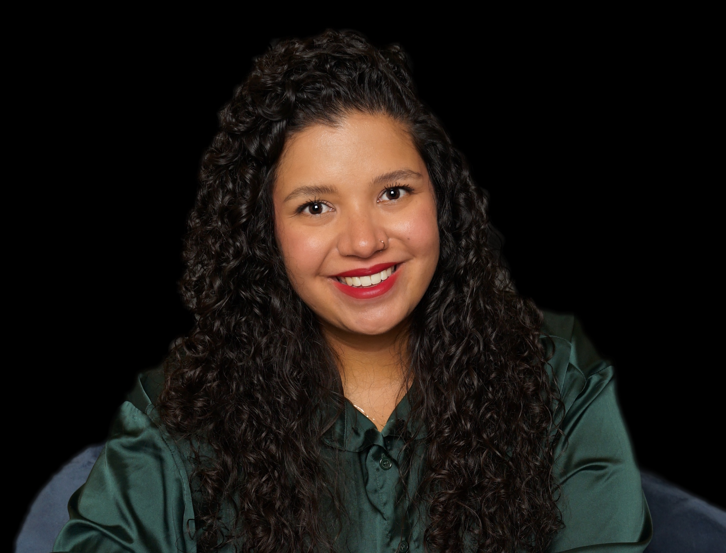 Portrait of a woman with long curly dark hair, smiling, wearing a green satin shirt, against a black background.