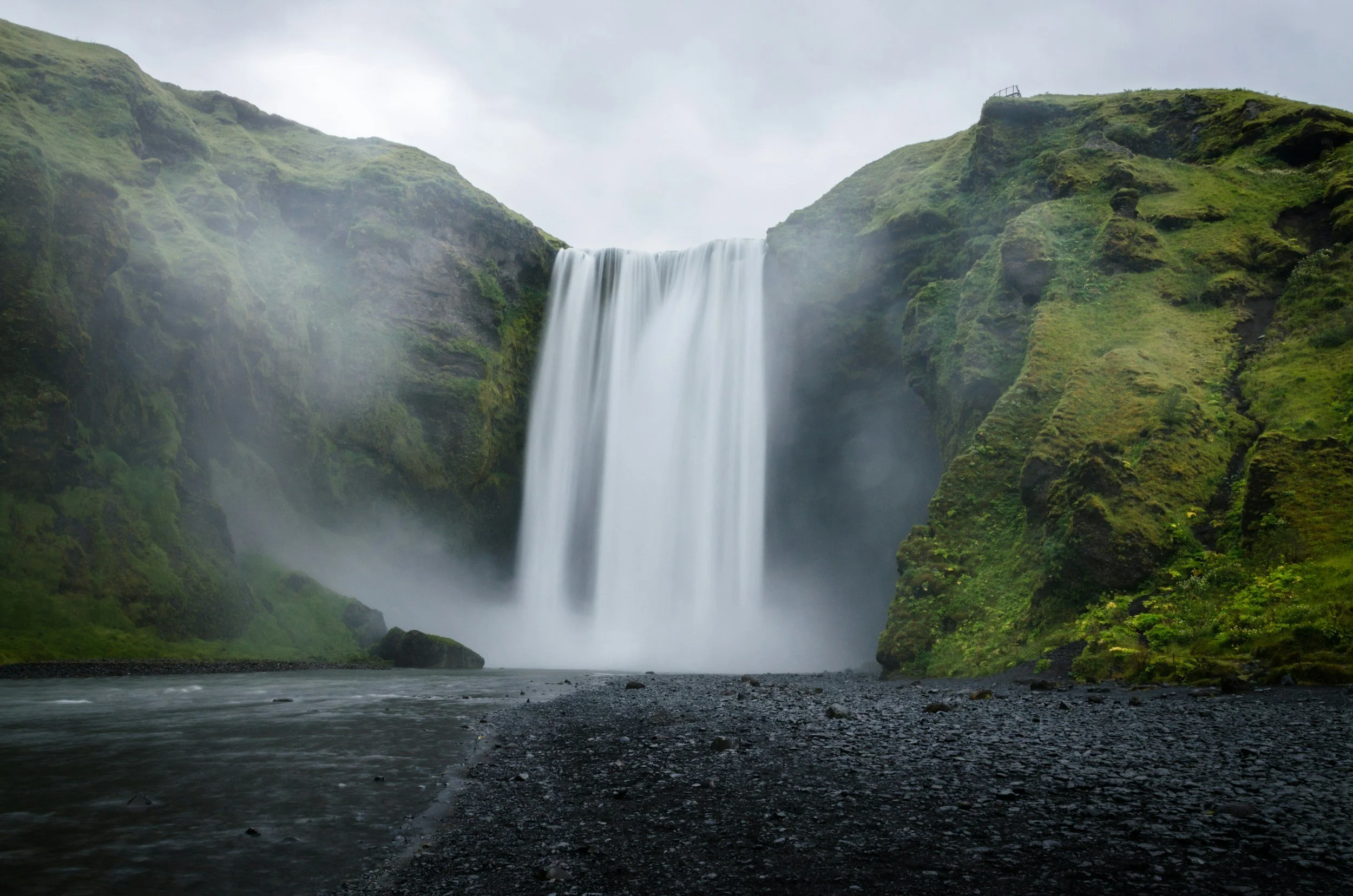 Skógafoss waterfall on Iceland’s South Coast cascading between lush green cliffs into a misty river below