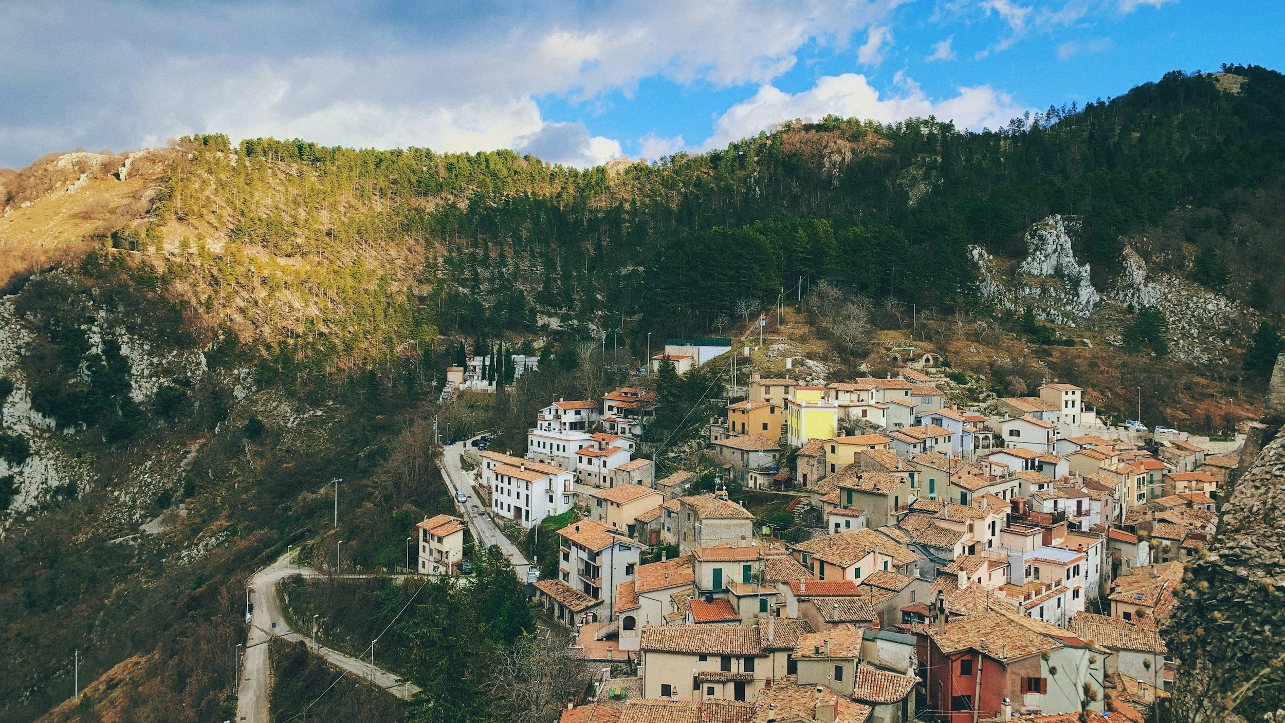 Hilltop village with terracotta rooftops nestled in the mountains of Abruzzo, Italy surrounded by forests and winding roads.