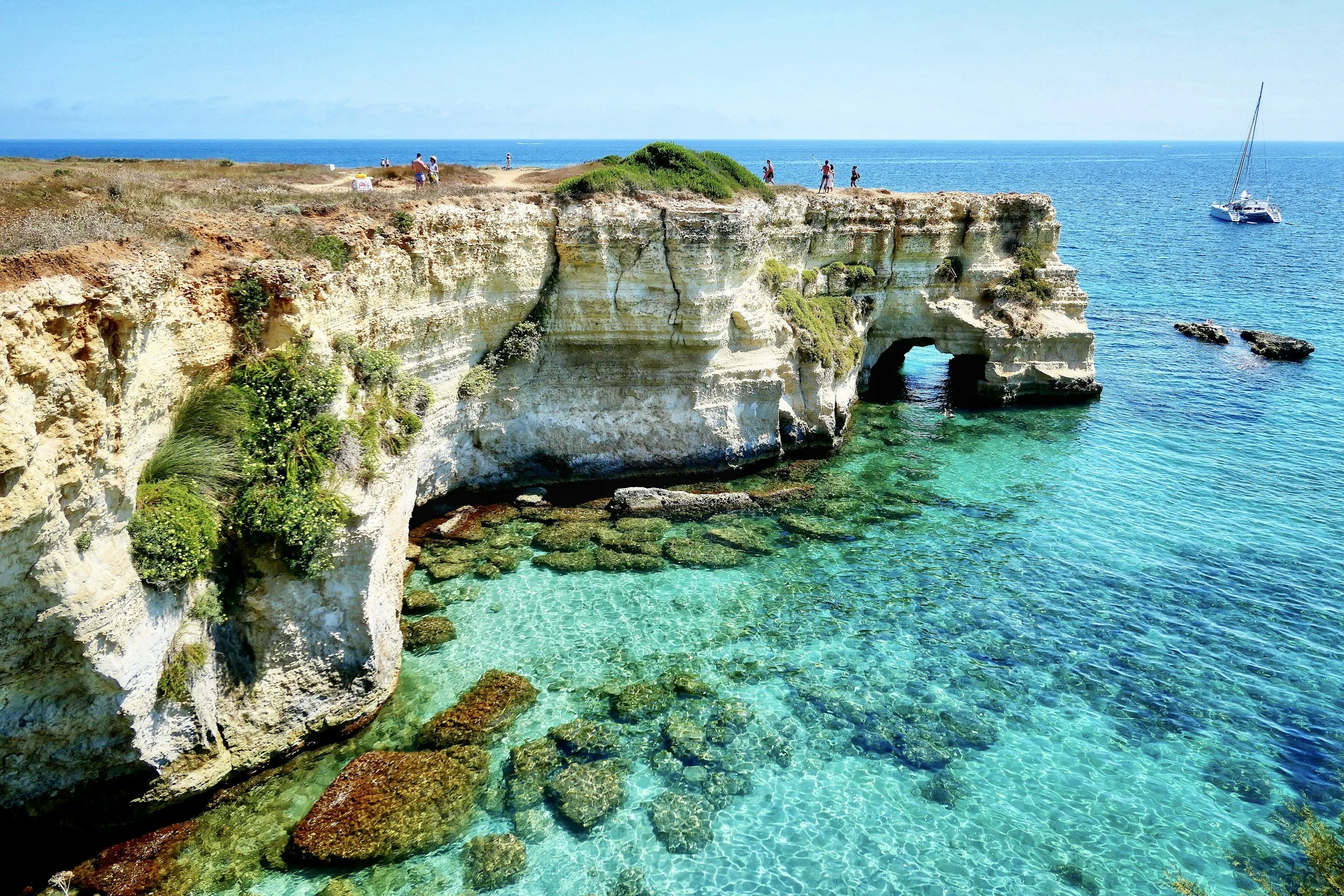 Rocky limestone cliffs and sea cave overlooking crystal-clear turquoise waters along the coastline of Puglia, Italy.