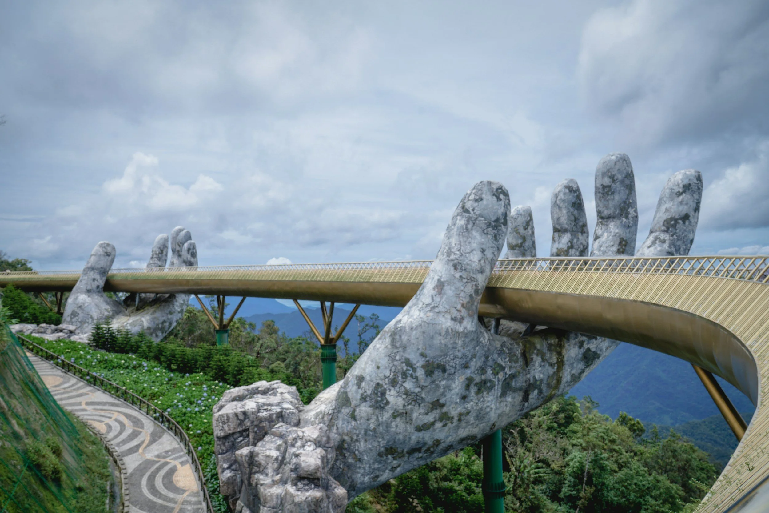 Golden Bridge in Ba Na Hills, Vietnam held by giant stone hands overlooking lush mountains and misty sky.
