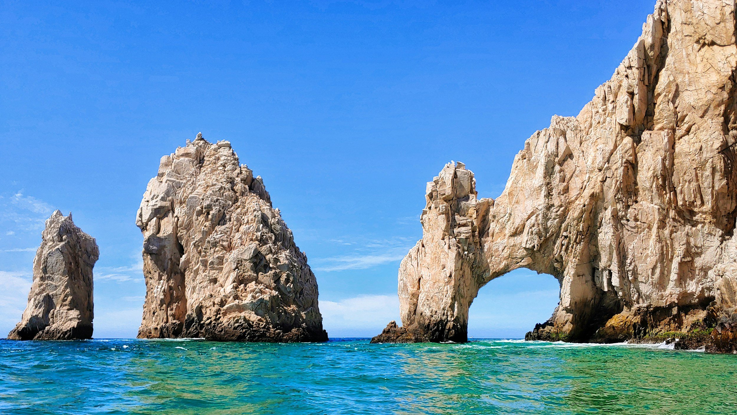 Beautiful rock formations at El Arco in Cabo San Lucas with turquoise ocean water and dramatic coastal cliffs under a clear blue sky.