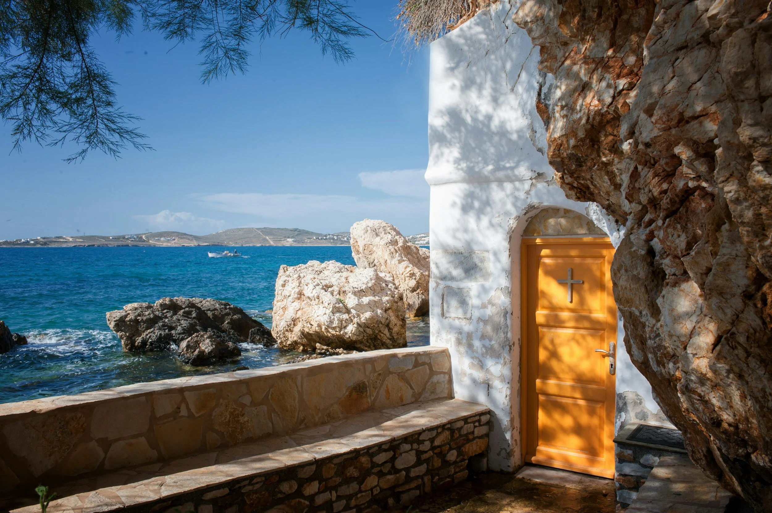 Seaside chapel carved into rocky coastline with a bright yellow door overlooking the Aegean Sea in Greece