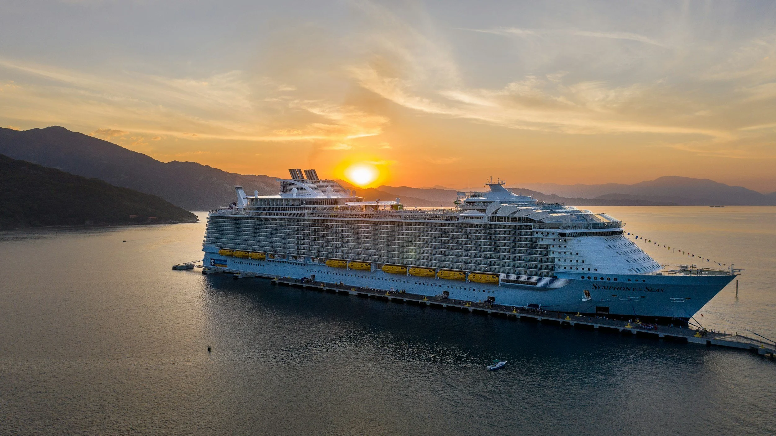 Royal Caribbean Symphony of the Seas cruise ship docked at sunset with mountains and ocean in the background