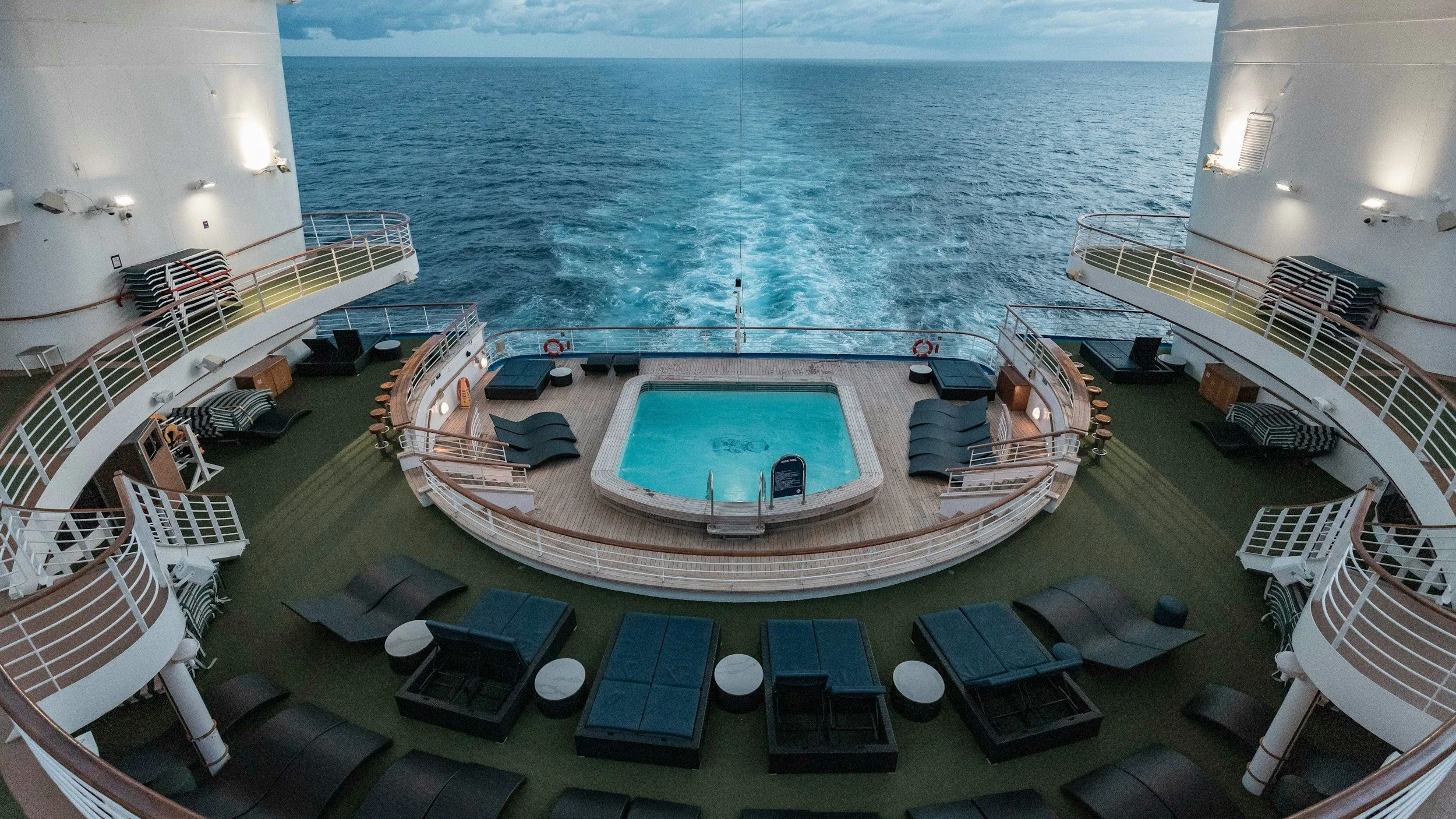 Cruise ship pool deck at the stern with lounge chairs overlooking the open ocean wake