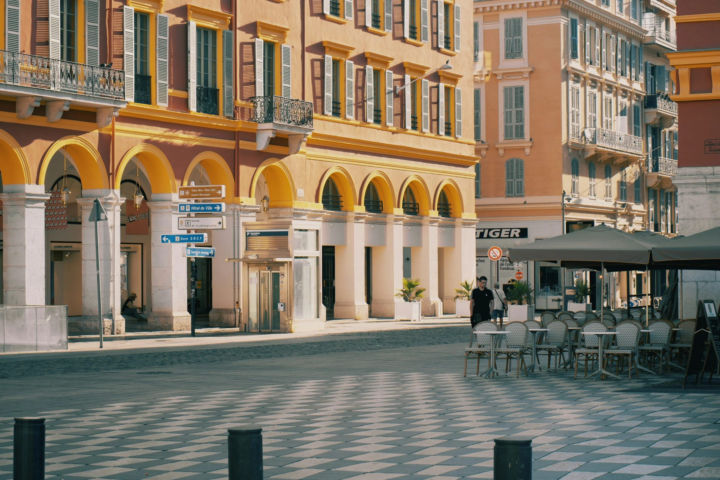 Colorful historic buildings and café seating in a sunlit square in Nice, France