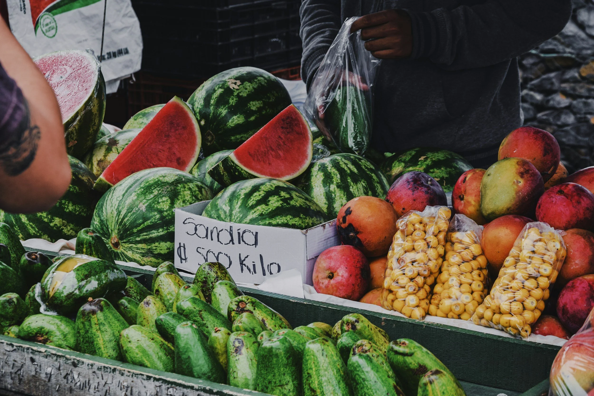 Colorful produce stand at a Costa Rican farmers market featuring fresh watermelon, mangoes, avocados, and local fruits, showcasing the vibrant flavors and agricultural abundance of the country.