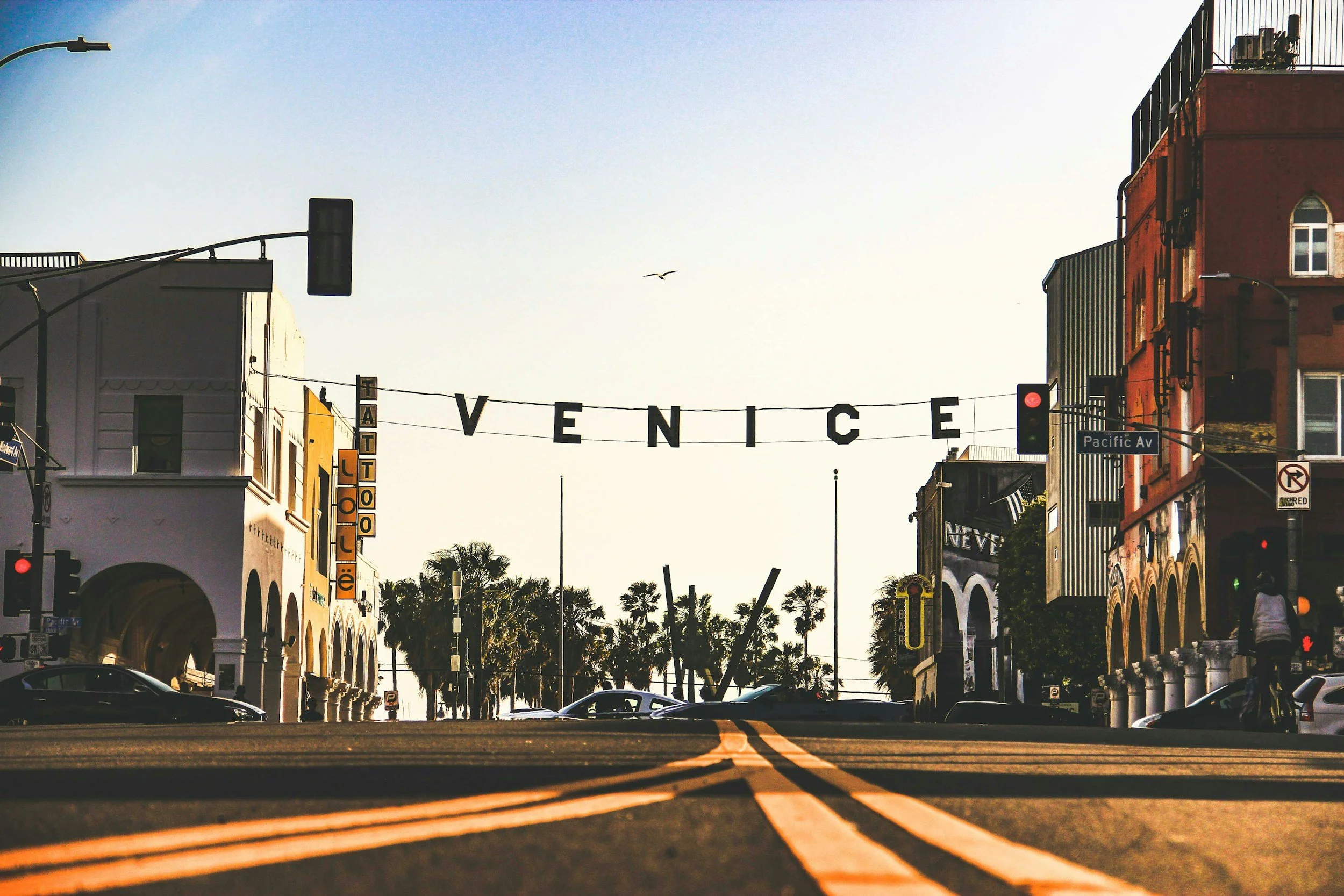 The iconic Venice sign stretches across a palm-lined street in Venice Beach, Los Angeles, as the neighborhood's eclectic shops, murals, and coastal atmosphere capture the laid-back spirit of Southern California.