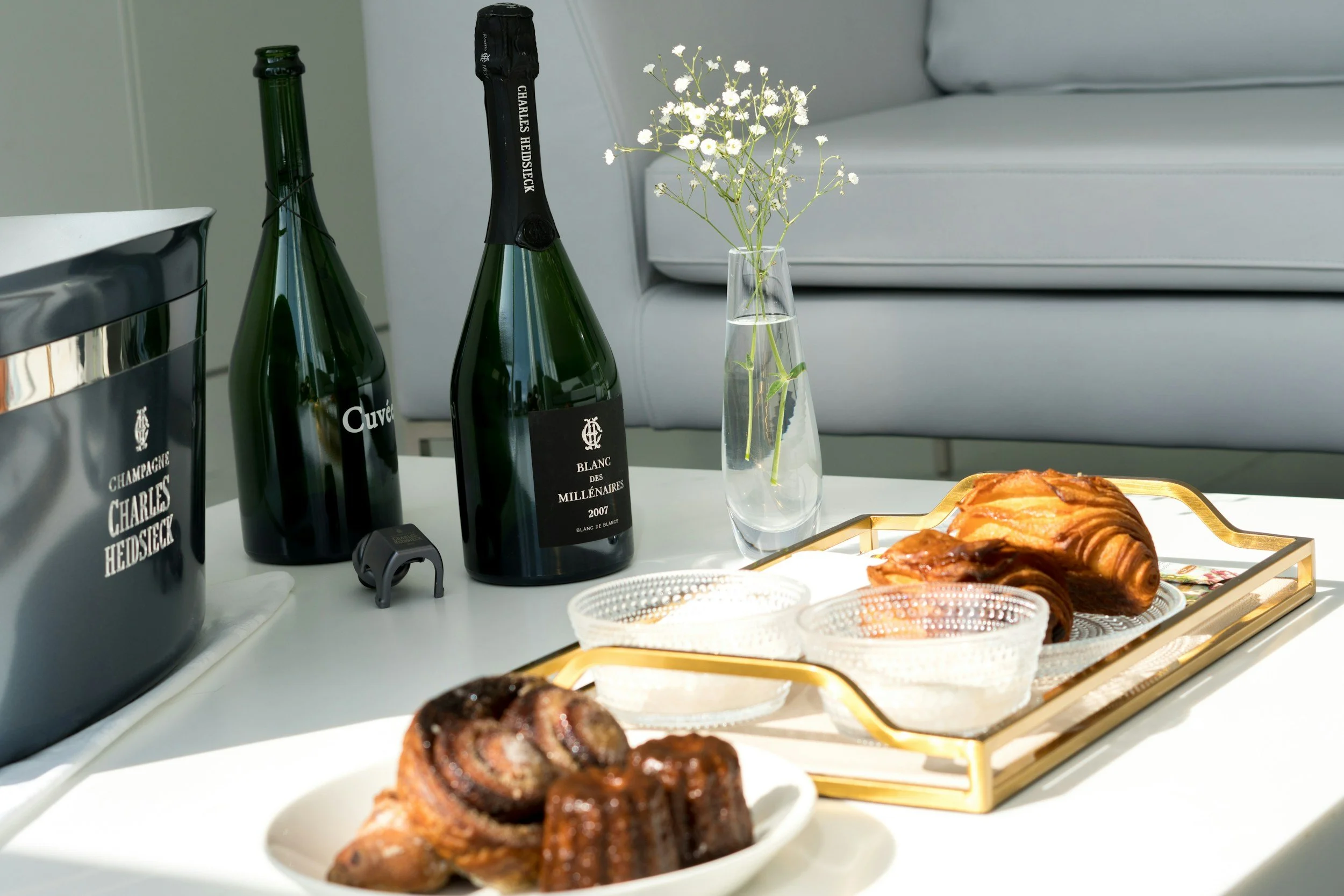 Luxury champagne service with Charles Heidsieck bottles, an ice bucket, fresh pastries, and delicate flowers arranged on a sunlit table.