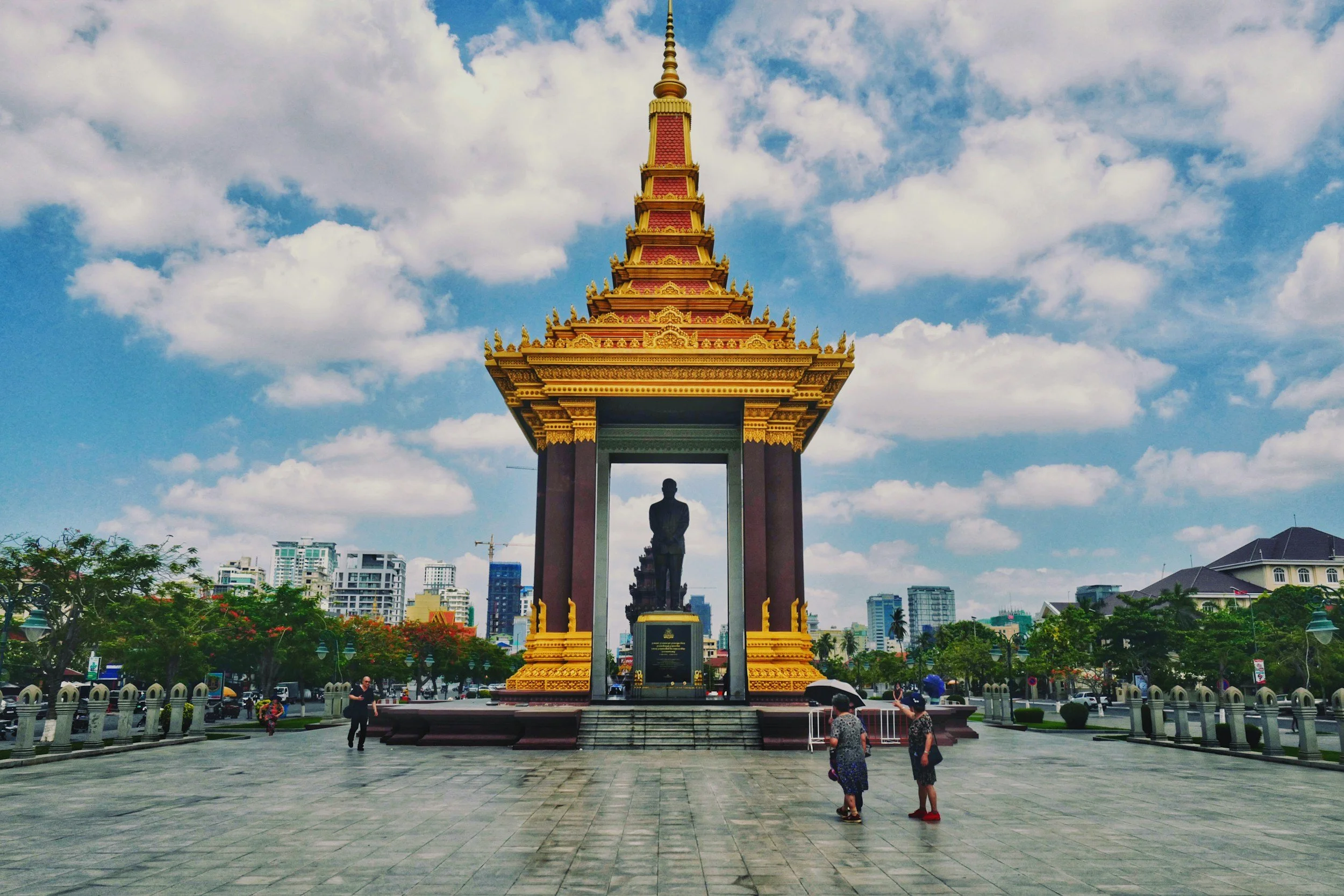 Independence Monument in Phnom Penh, Cambodia, featuring ornate Khmer architecture beneath a bright blue sky with the city skyline in the background.