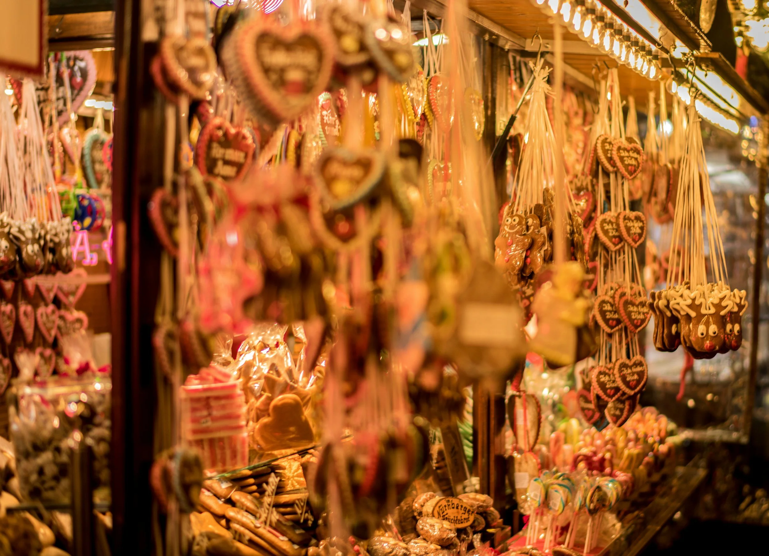 Traditional German Christmas market stall filled with heart-shaped gingerbread cookies, colorful candies, and festive sweets illuminated by warm holiday lights.