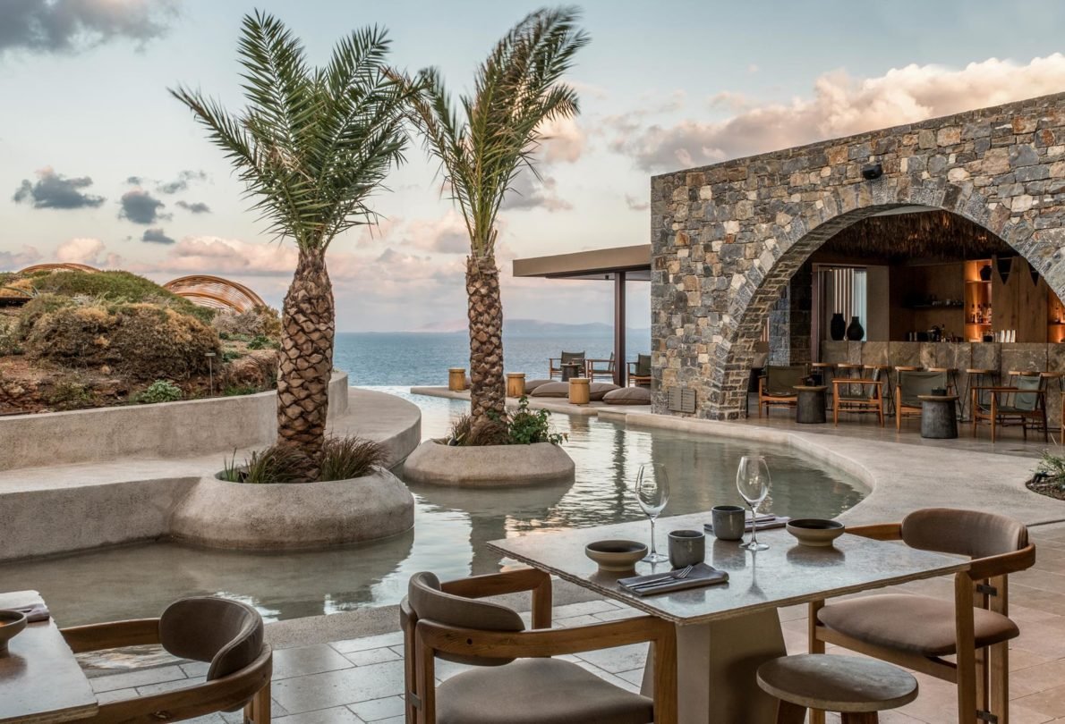 Oceanfront dining area at Acro Suites in Crete featuring stone architecture, a tranquil lagoon-style pool, and panoramic sea views—ideal for luxury wellness and Mediterranean escapes.