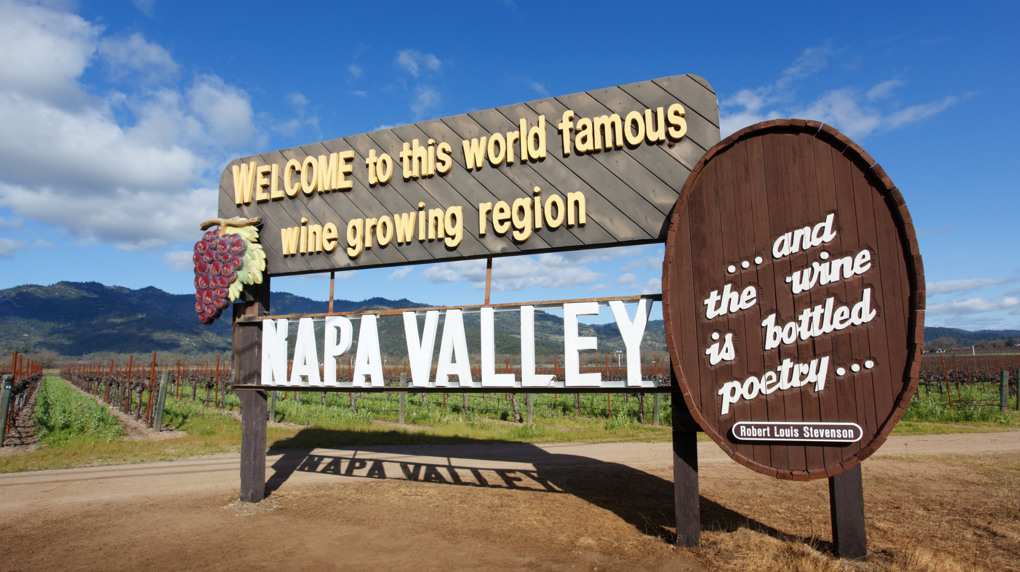 Welcome to Napa Valley sign surrounded by vineyards, welcoming visitors to California's world-famous wine region with rolling hills and vineyard rows in the background.