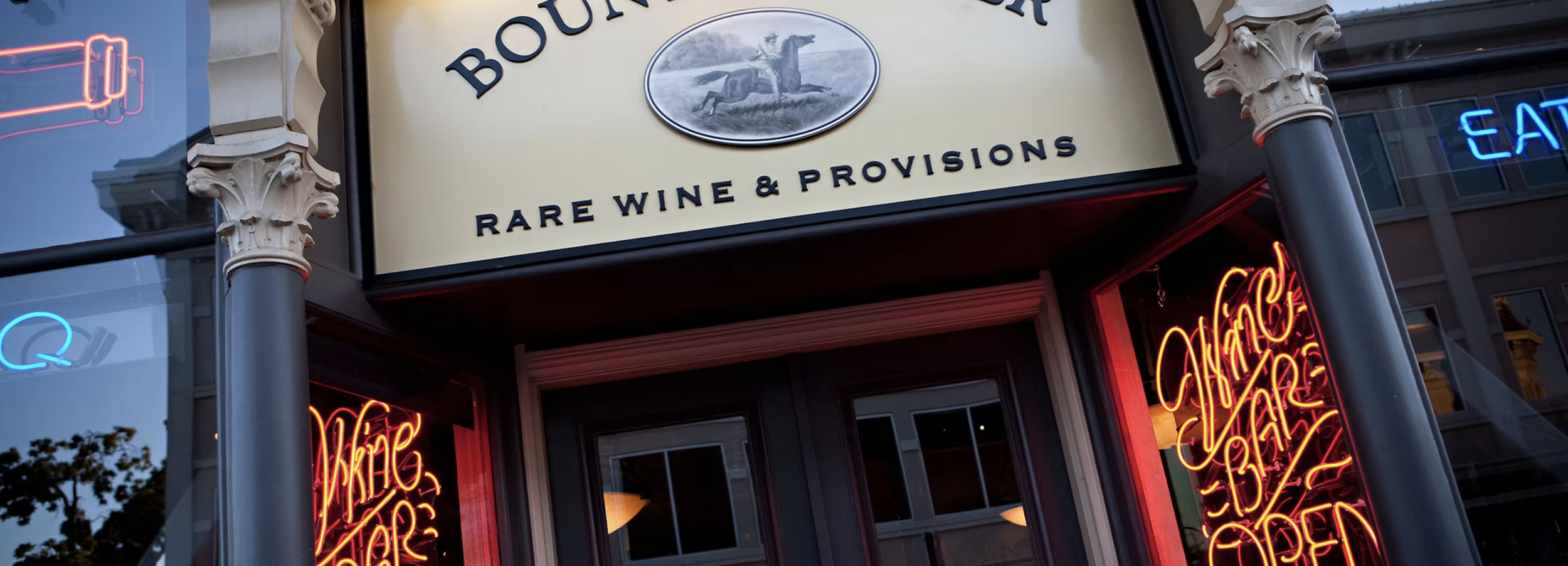 Exterior of Bounty Hunter Wine Bar & Smokin' BBQ in downtown Napa, featuring vintage storefront architecture, neon wine signs, and a specialty wine and provisions shop.