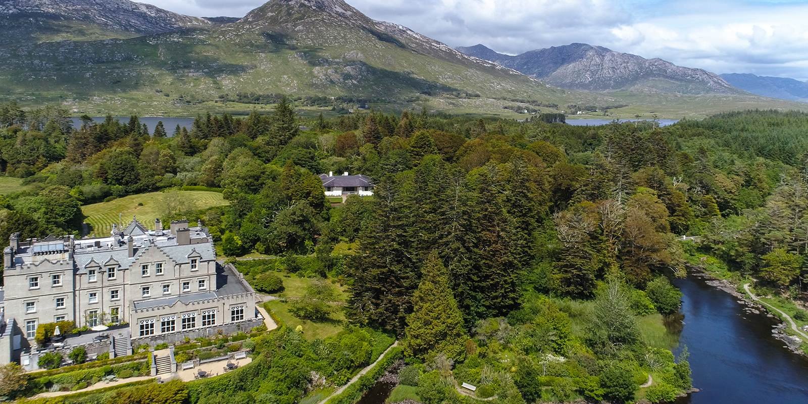 Ballynahinch Castle Hotel surrounded by lush gardens, forest, and river with scenic mountains in Connemara, Ireland.