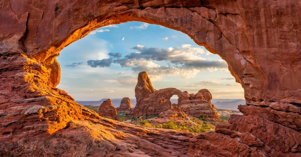 View through a natural sandstone arch in Arches National Park, Utah showcasing red rock formations and desert landscape at sunset