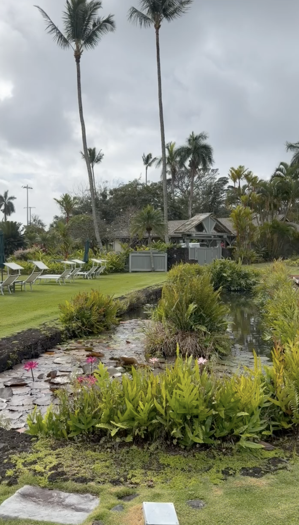 Outdoor spa grounds at Hana-Maui Resort featuring a tranquil koi pond, tropical landscaping, palm trees, and serene relaxation area on Maui’s east coast.