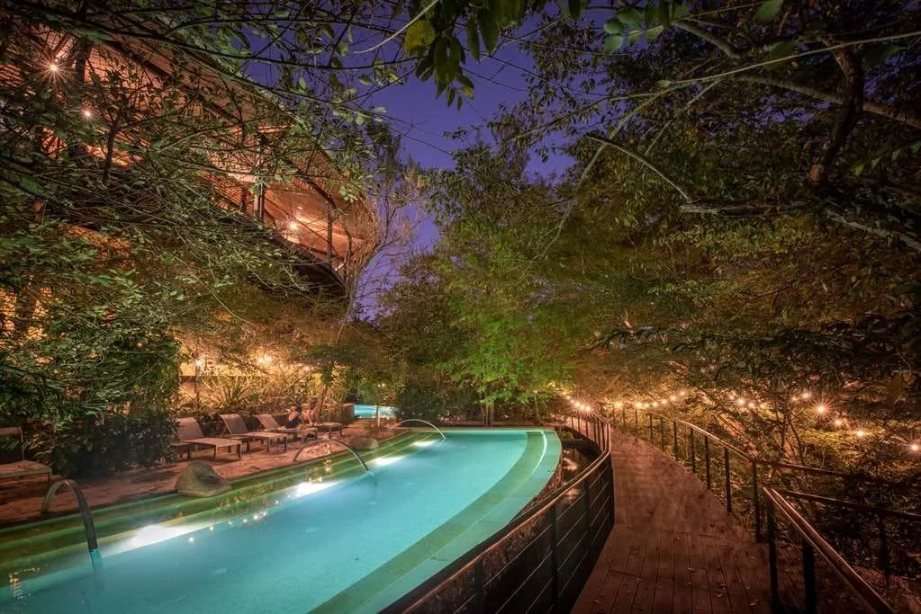 Serene thermal pool winding through the forest at Rio Perdido Hotel & Thermal River in Costa Rica, illuminated by warm lights and surrounded by lush tropical vegetation at dusk.