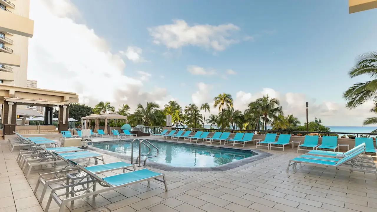 Pool deck at Hyatt Regency Waikiki Beach Resort & Spa featuring lounge chairs, tropical palm trees, and ocean views near Waikiki Beach in Honolulu, Oahu, Hawaii.