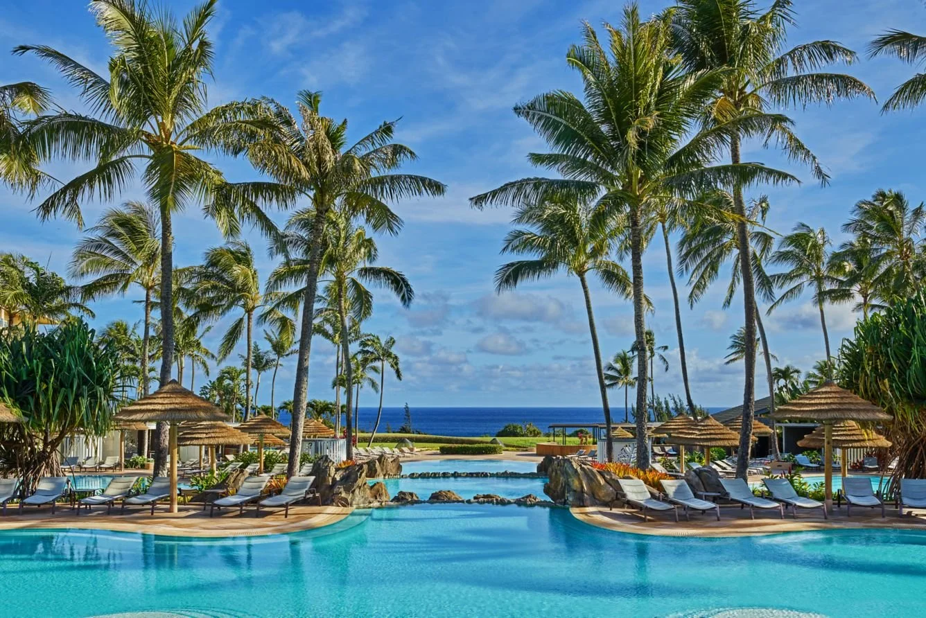 Pool area at The Ritz-Carlton Kapalua surrounded by palm trees with ocean views and lounge chairs in Maui, Hawaii