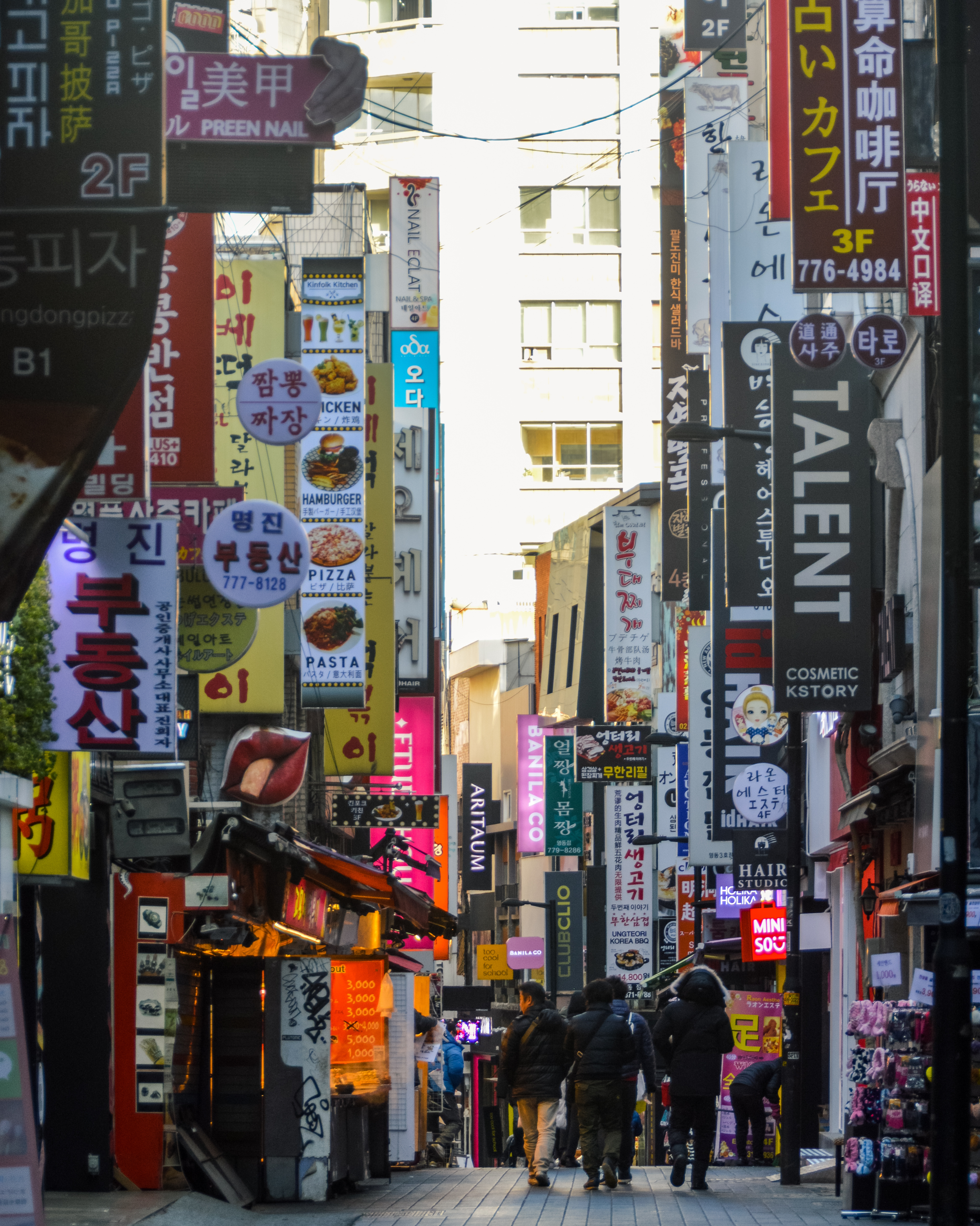 Busy shopping street in Seoul, South Korea with colorful storefront signs, restaurants, and vibrant city street life.
