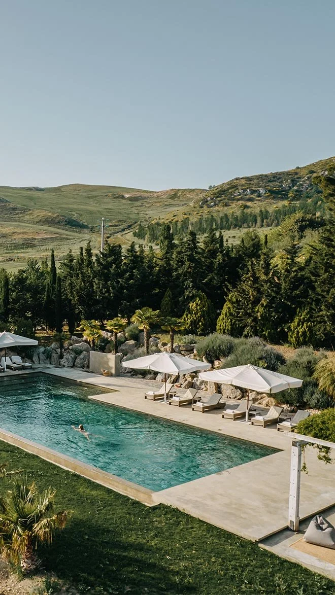 Countryside pool surrounded by rolling green hills and Mediterranean gardens at Masseria Susafa in Sicily—perfect for a peaceful rural retreat in Italy.