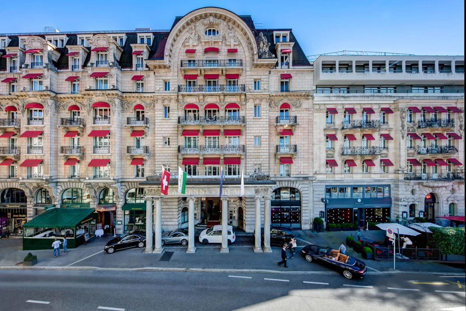 Elegant historic hotel façade in Lausanne with red awnings and Swiss flags along a grand city street in Switzerland