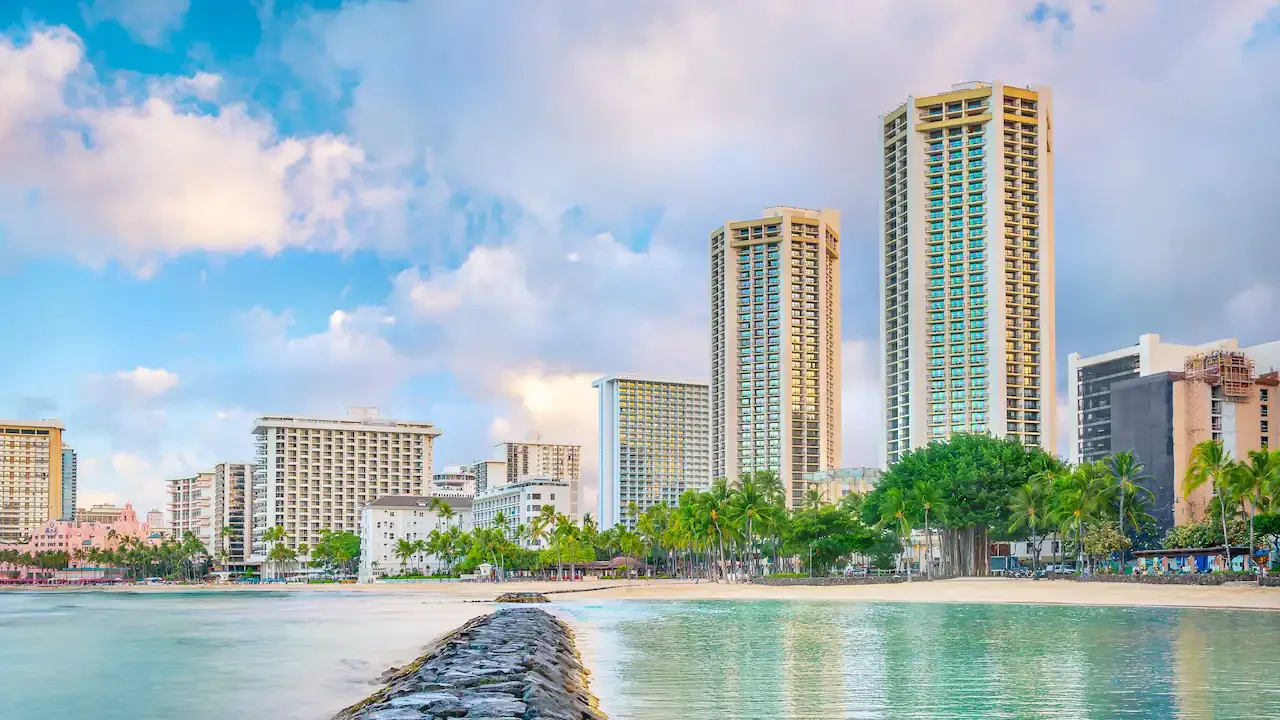 Hyatt Regency Waikiki Beach Resort & Spa towers viewed from the ocean along Waikiki Beach with Honolulu skyline and palm-lined shoreline in Oahu, Hawaii.