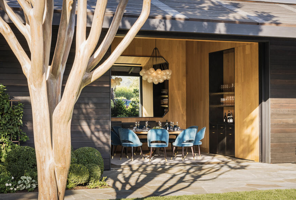 Modern Napa Valley winery tasting room featuring indoor-outdoor seating, contemporary architecture, elegant blue chairs, and a private wine tasting table overlooking landscaped gardens.