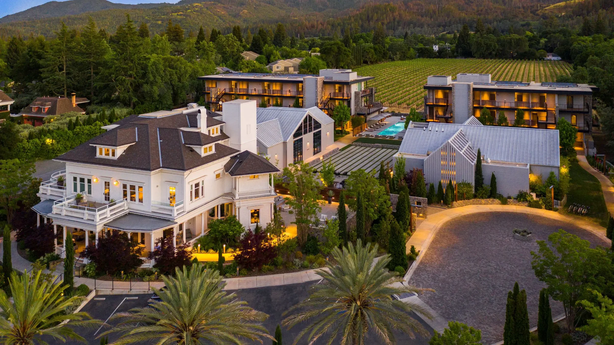 Aerial view of a luxury Napa Valley resort surrounded by vineyards, featuring elegant guest accommodations, a historic mansion, landscaped grounds, and a central outdoor pool.