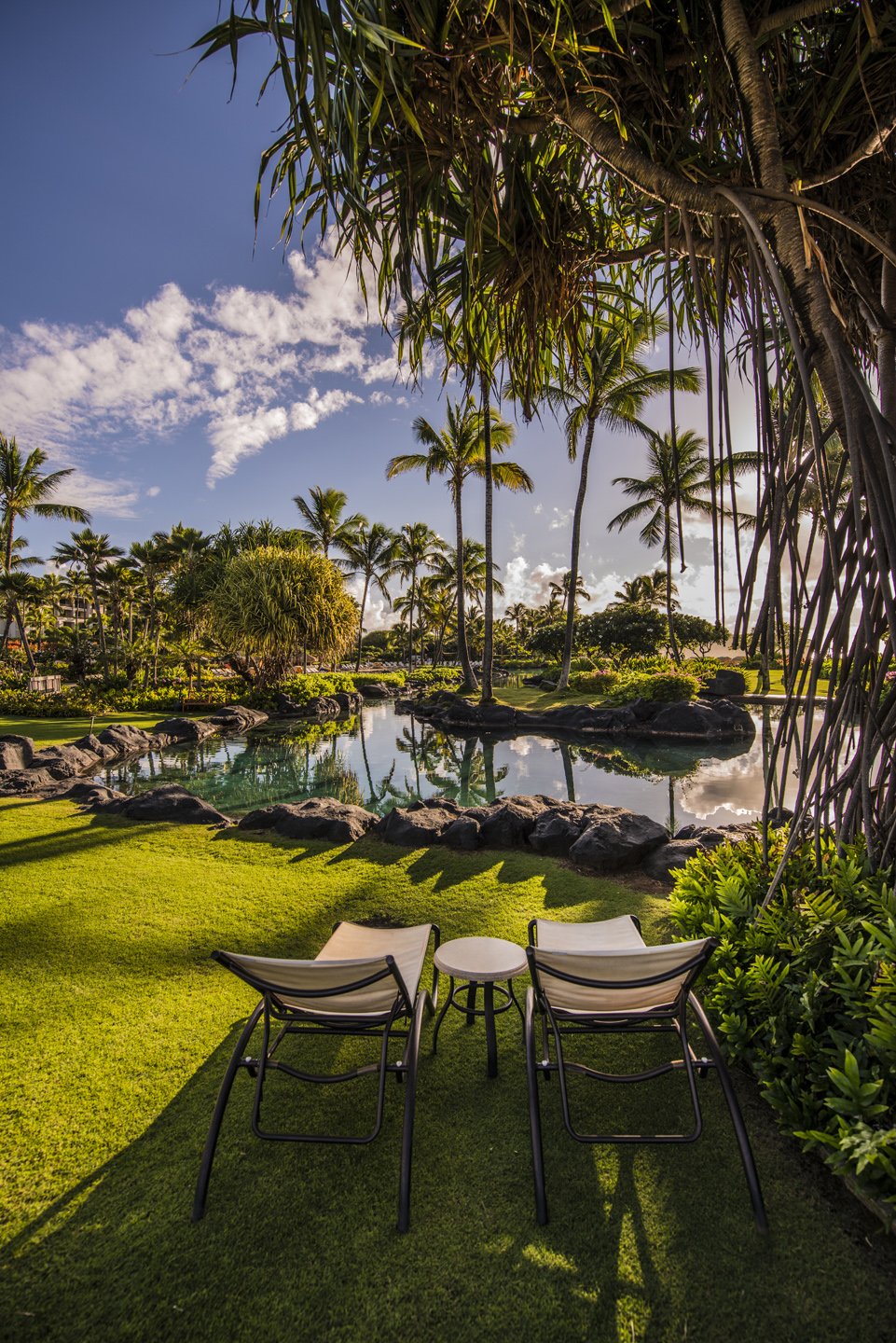 Peaceful lagoon and tropical gardens at Grand Hyatt Kauai Resort & Spa in Poipu, Hawaii featuring palm trees, reflective water, and lounge chairs overlooking the lush resort grounds.