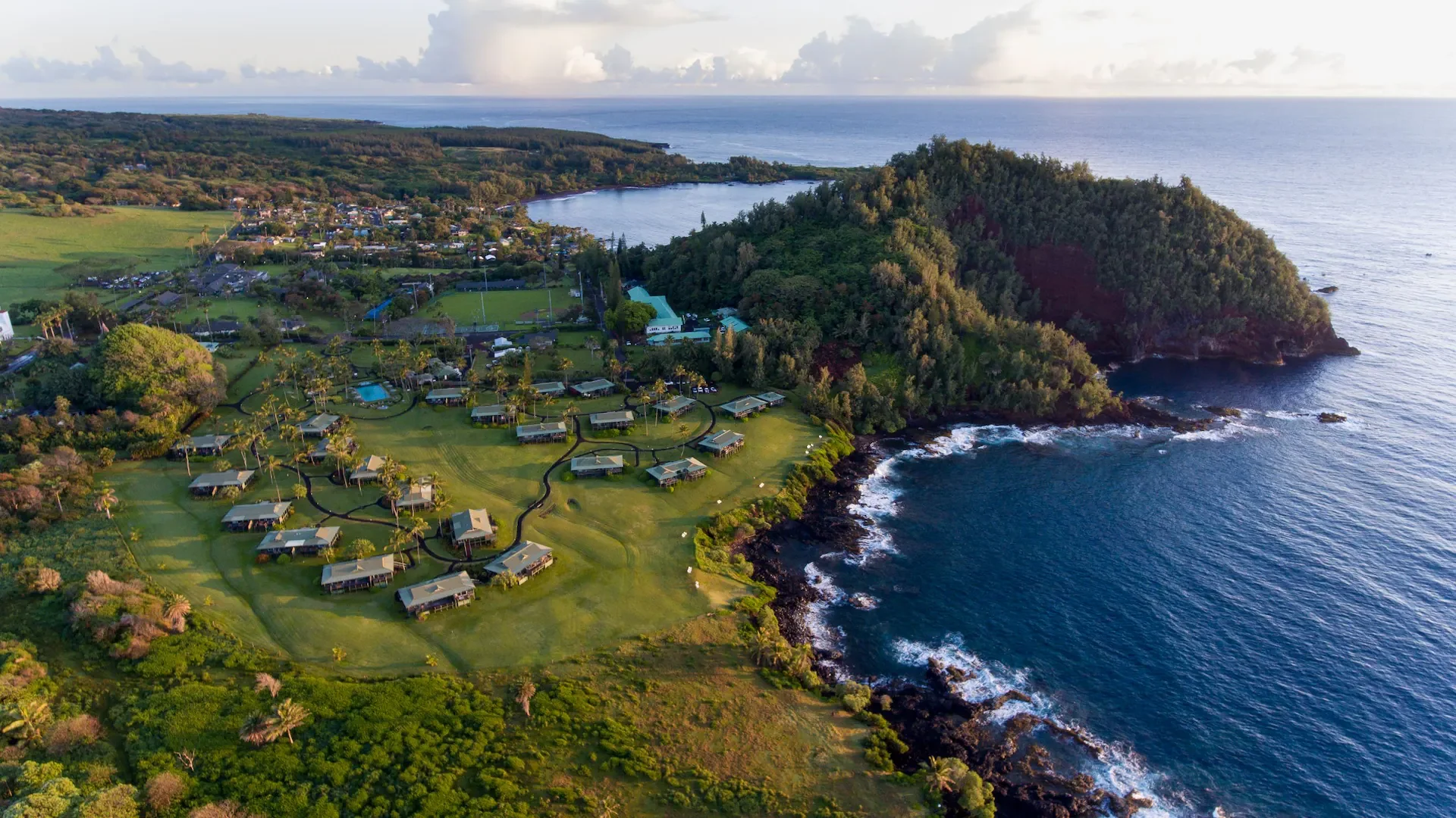 Aerial view of Hana-Maui Resort on Maui’s rugged coastline with oceanfront bungalows, lush greenery, and dramatic cliffside views.