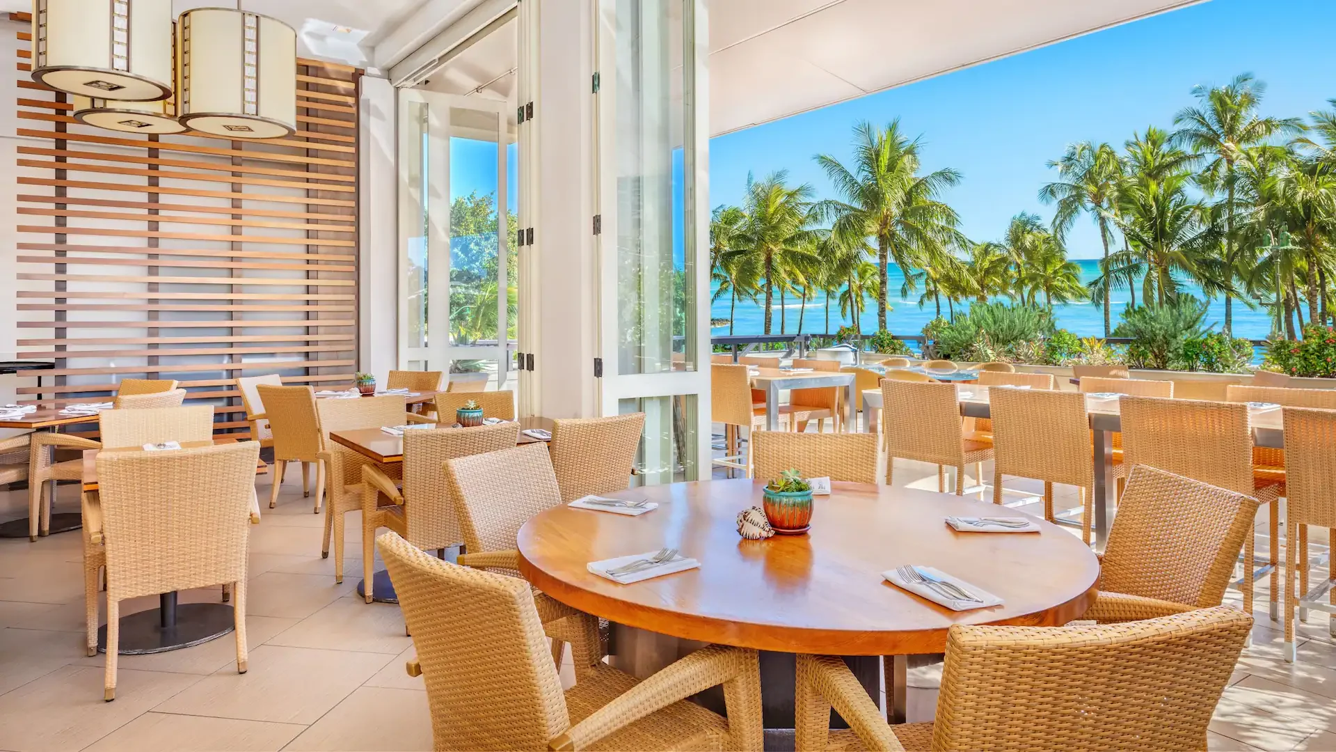 Open-air dining at Hyatt Regency Waikiki Beach Resort & Spa restaurant overlooking palm trees and the Pacific Ocean at Waikiki Beach in Honolulu, Oahu.