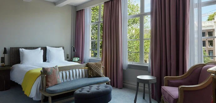 Pulitzer Amsterdam hotel room with large windows, canal views, soft pink accents, and elegant boutique-style furnishings.