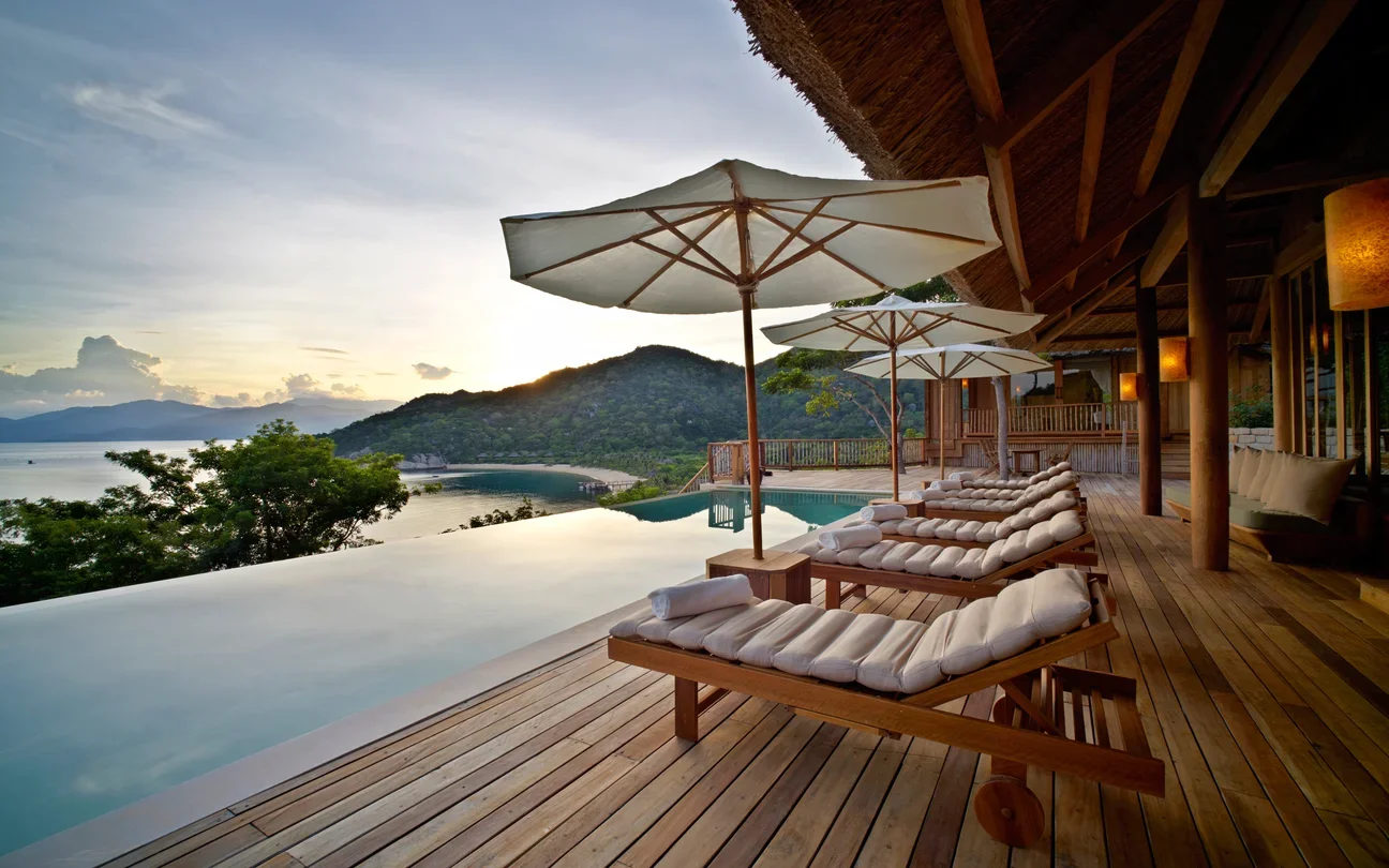 Luxury villa at Six Senses Ninh Van Bay featuring an infinity pool, wooden sun loungers, and panoramic ocean views at sunset.