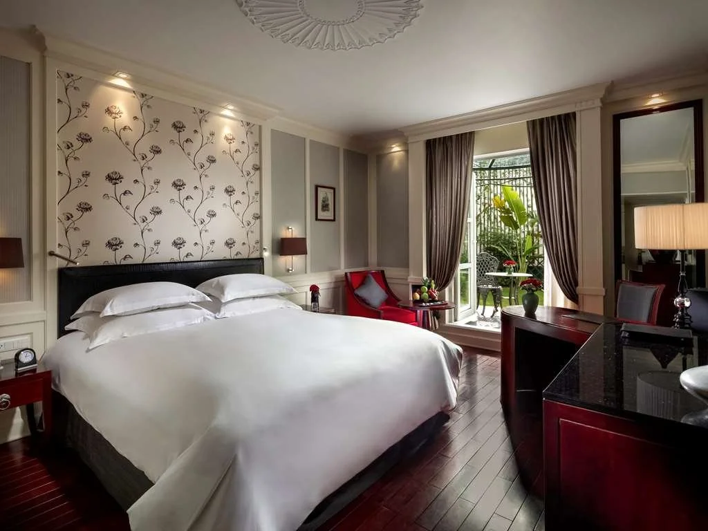 Elegant guest room at Sofitel Hanoi featuring a plush king bed, classic French colonial design, and balcony overlooking a lush garden.