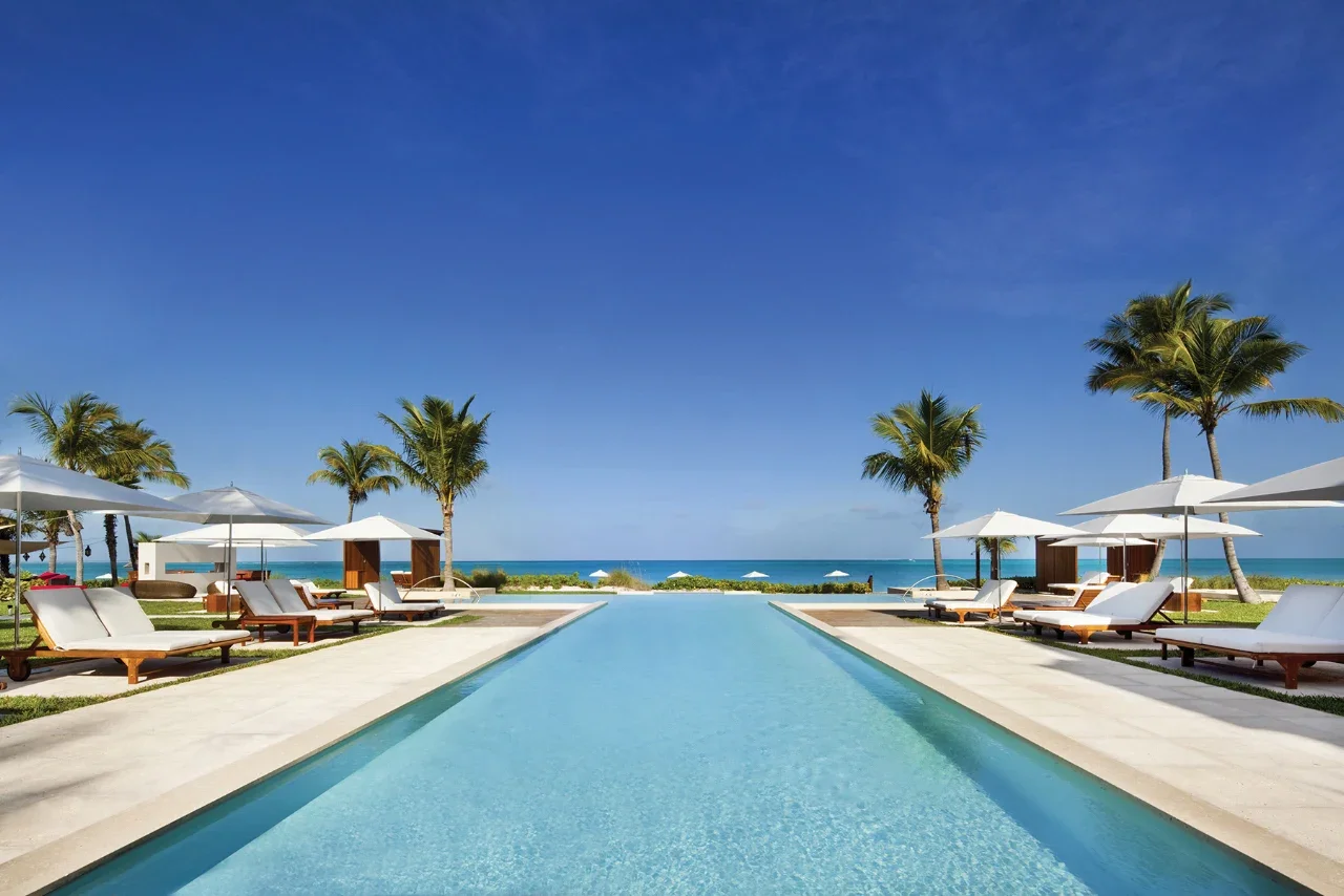 Infinity pool at Grace Bay Club in Turks & Caicos with ocean views, palm trees, and beachfront loungers—perfect for a luxury Caribbean beach getaway.