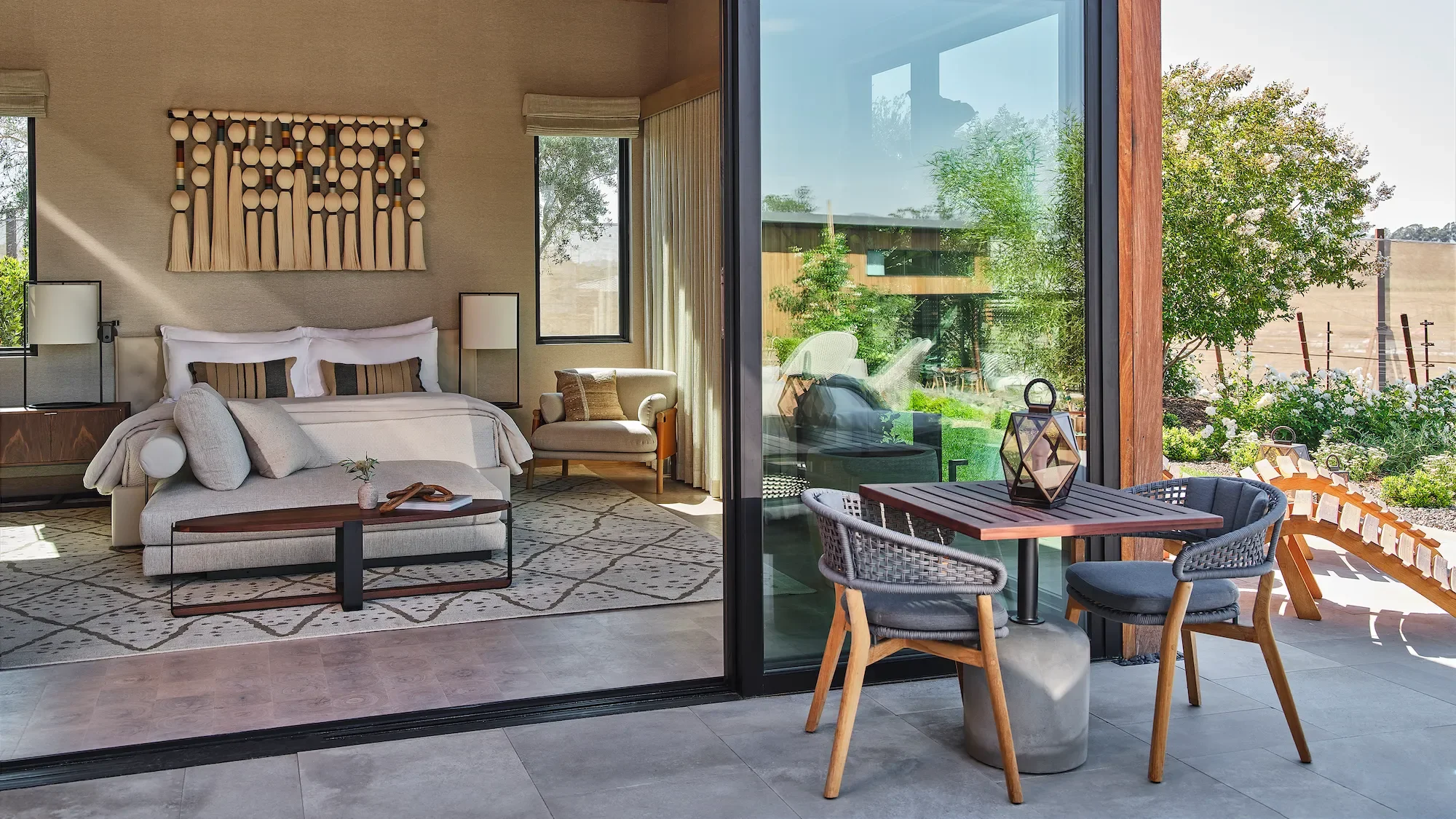 Luxury guest room in Napa Valley featuring a king bed, contemporary furnishings, a private outdoor patio, and floor-to-ceiling sliding glass doors overlooking landscaped gardens.