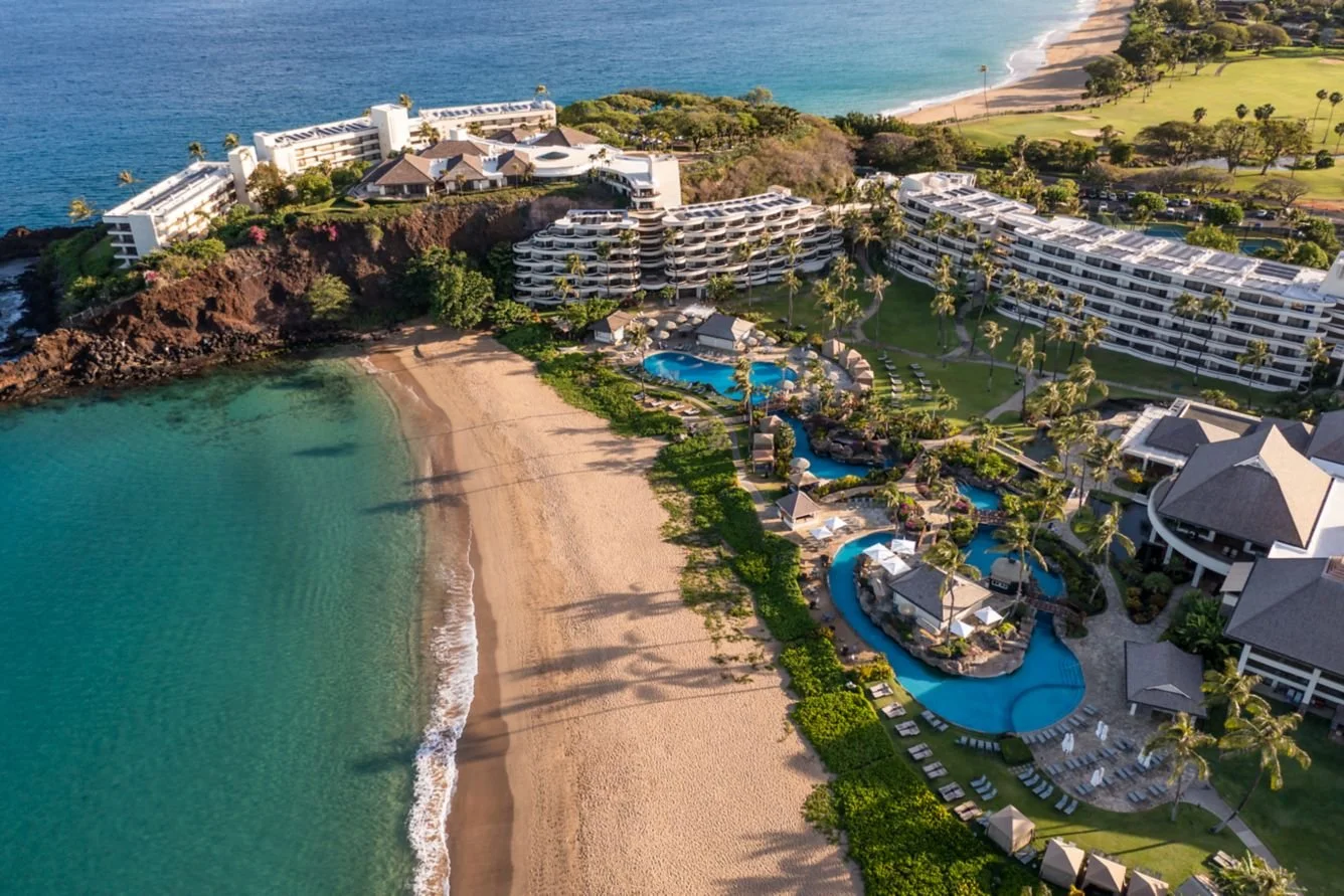 Wailea Beach Resort Maui aerial view with oceanfront pools, sandy beach, and lush tropical grounds along the coastline.
