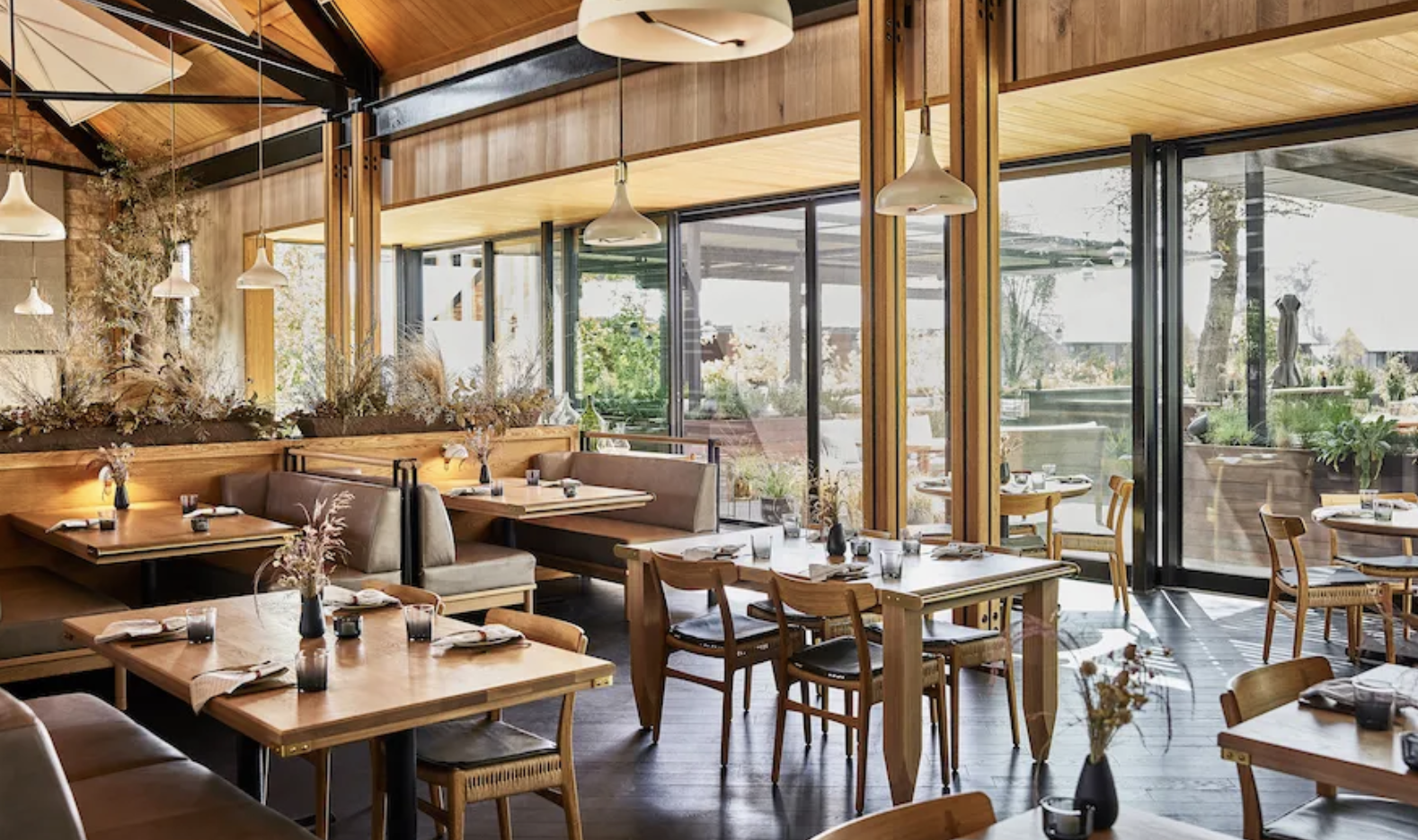Elegant Napa Valley restaurant dining room with warm wood interiors, floor-to-ceiling windows, and modern tables overlooking a lush outdoor garden.