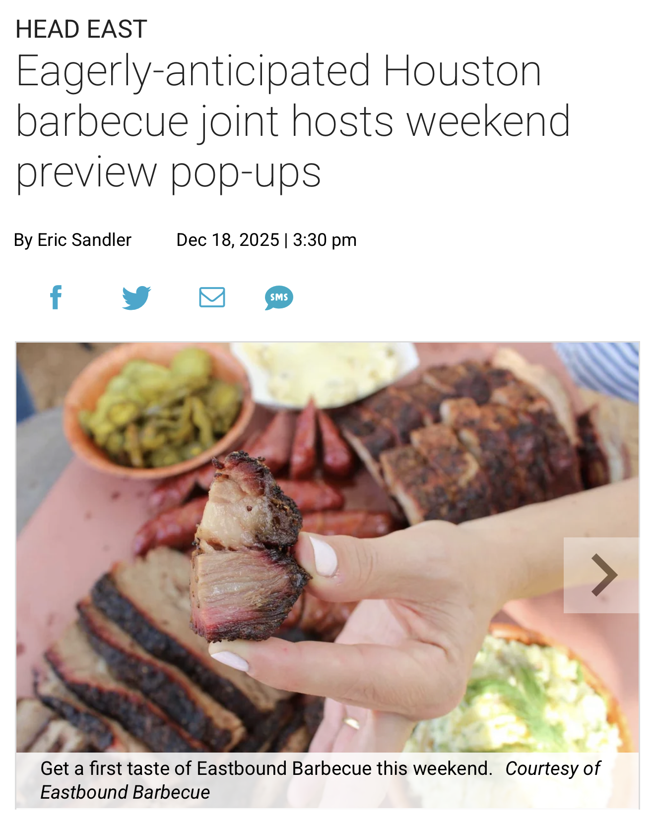 Close-up of a person holding a piece of barbecued brisket with a background of other barbecue dishes, including sliced brisket, and side dishes like pickles, potato salad, and sausage.