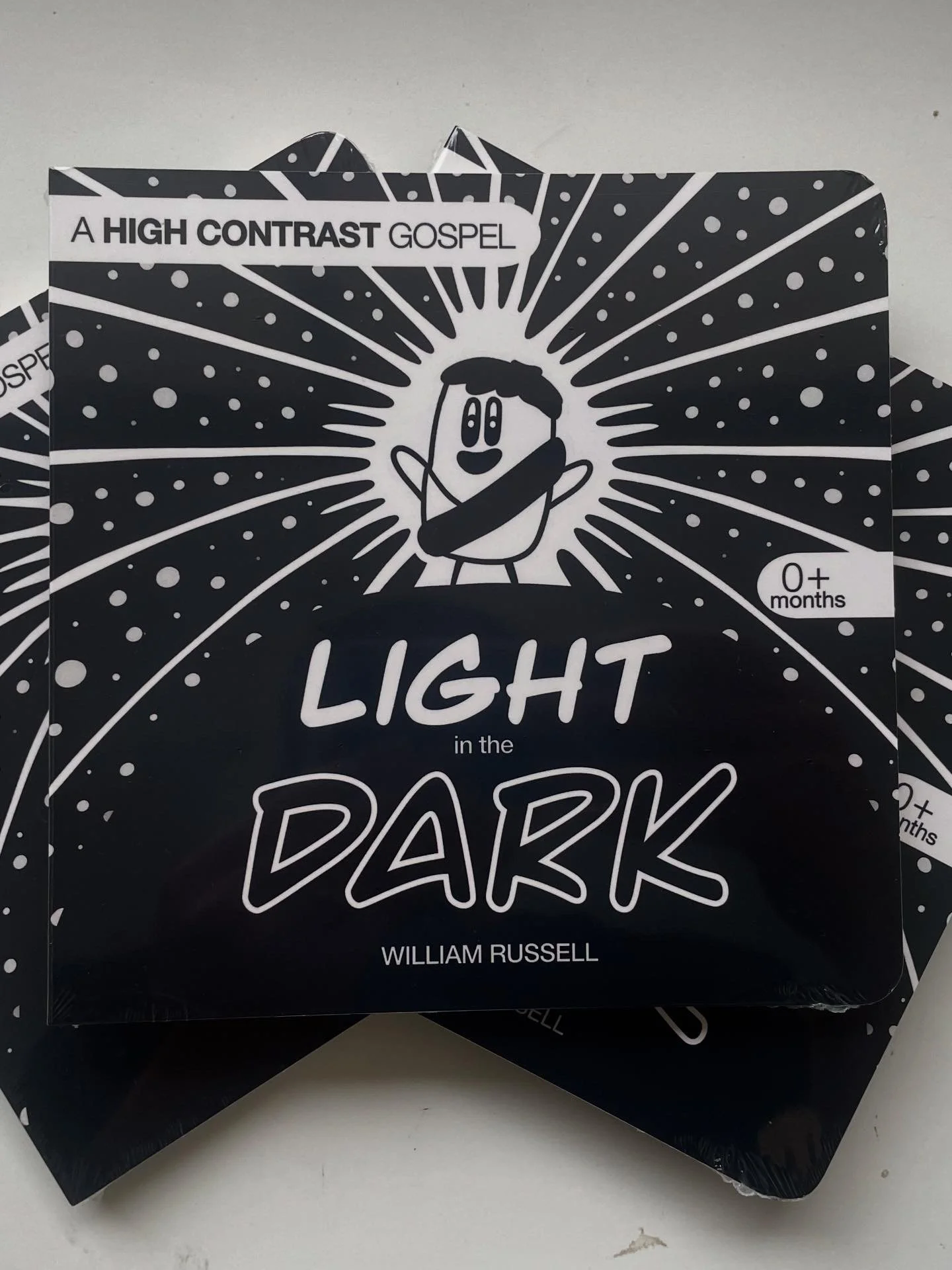 A book titled 'Light in the Dark' by William Russell, black and white cover with cartoon character, for ages 0+ months.