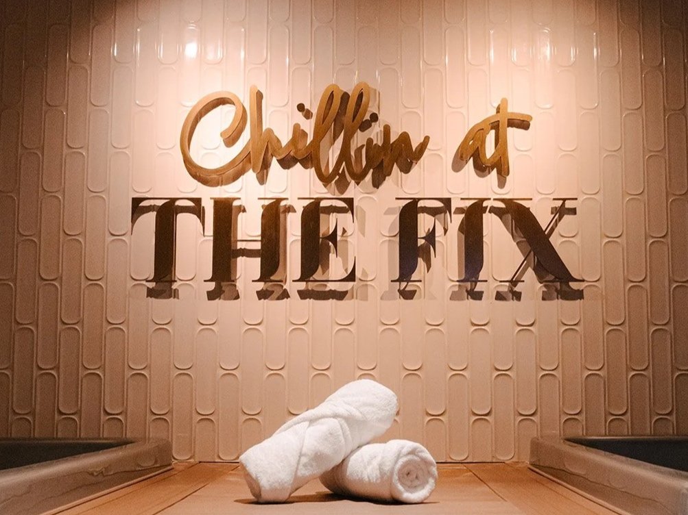 Towel art with two rolled white towels in front of a wall with the words 'Chillin at THE FIX' hanging on it, in a spa or wellness center setting.