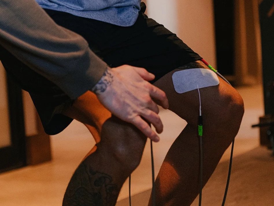 A person receiving physical therapy or a medical treatment on their leg, with an electrode pad attached to the thigh and wires connected to a device.