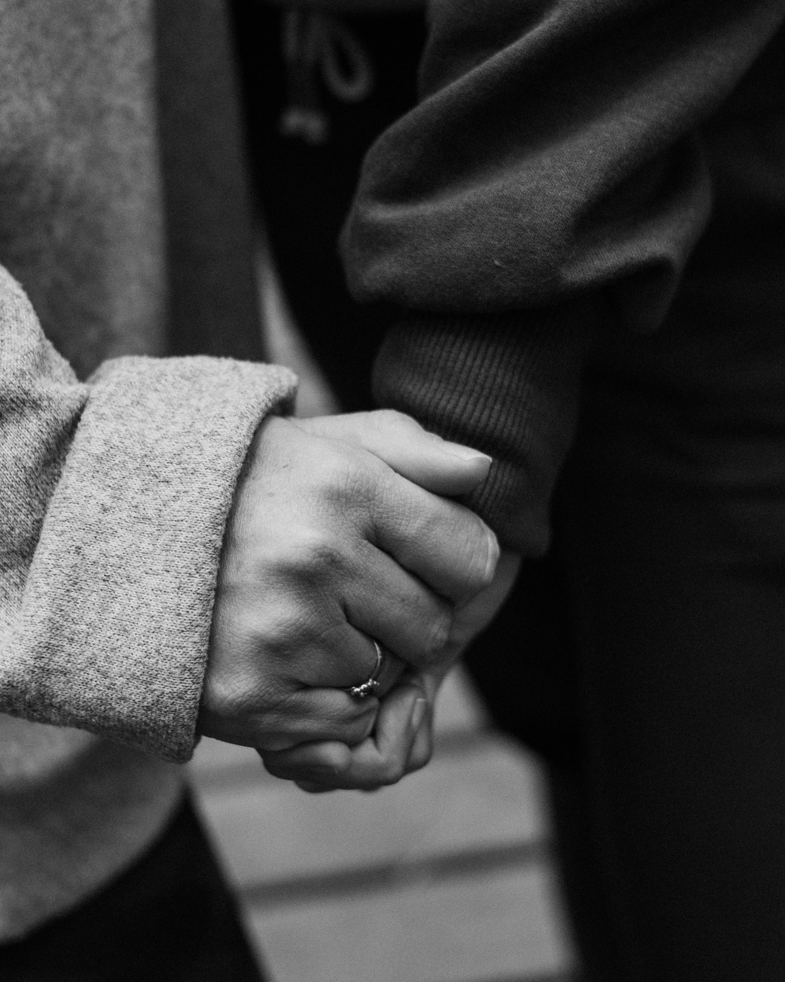 Close-up of two people holding hands, one wearing a ring, in black and white.