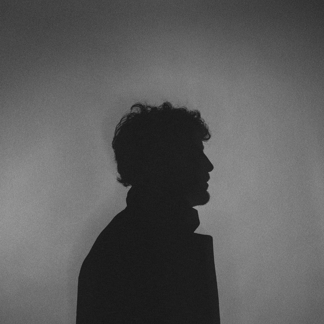 Silhouette of a man with curly hair and a beard against a plain background.